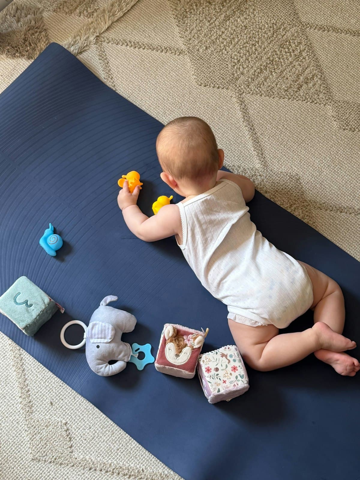 A baby doing tummy time on a play mat, reaching for toys