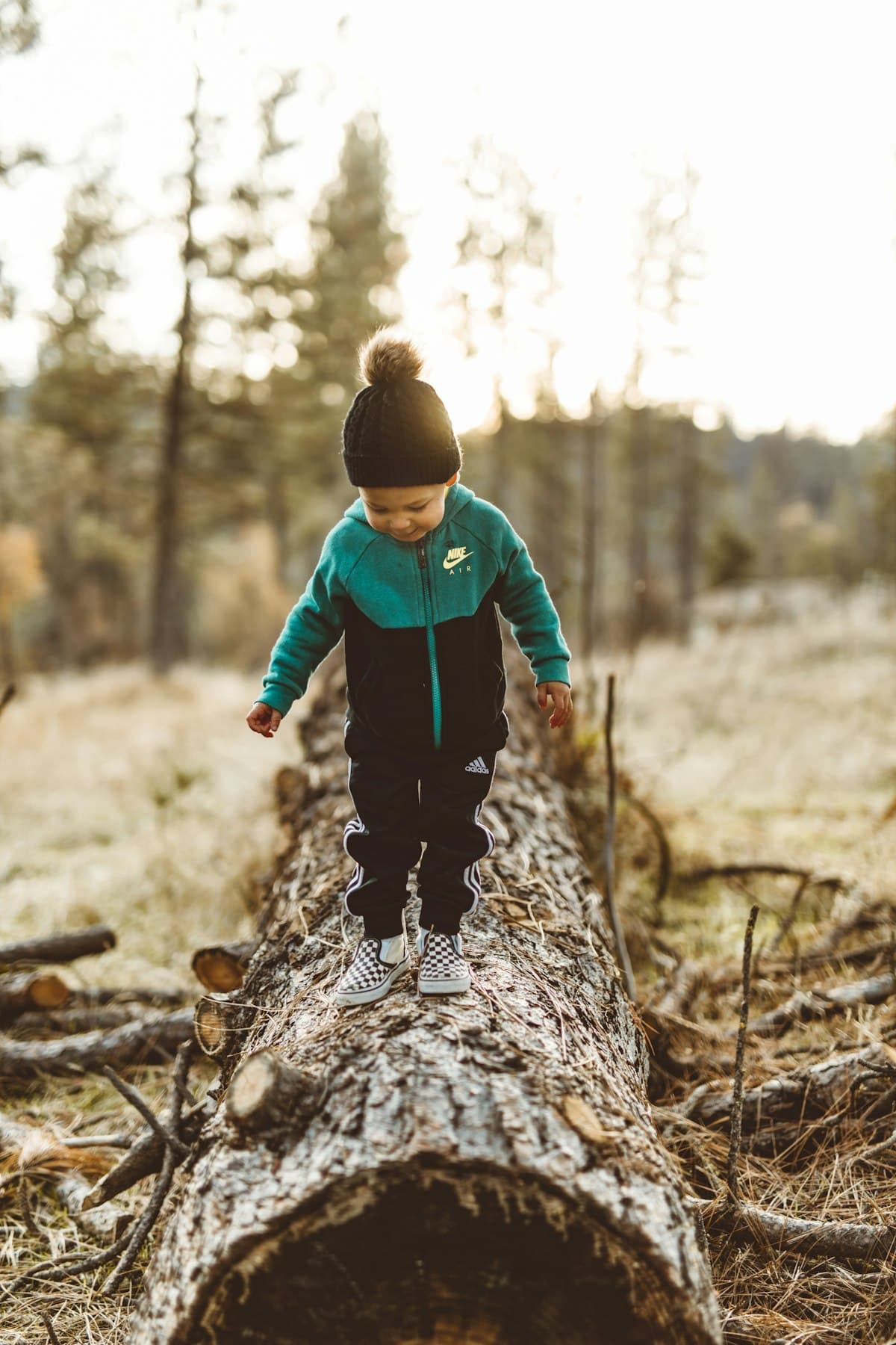 A young child in a bobble hat balancing along a fallen log in the woods