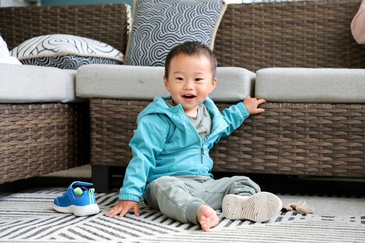 A smiling toddler sitting upright on a rug by the sofa