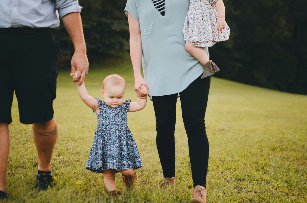 A toddler walking on grass, holding a parent's hand