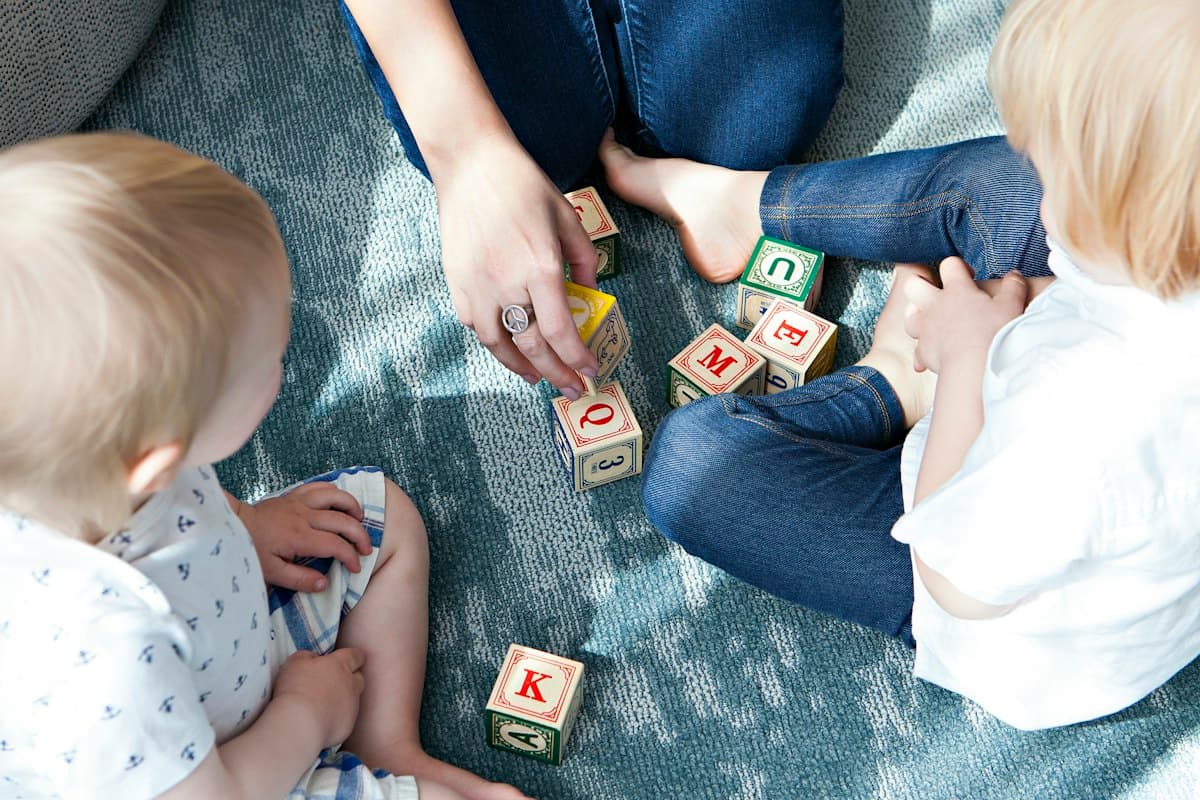 Two toddlers and a parent playing with letter blocks on a rug