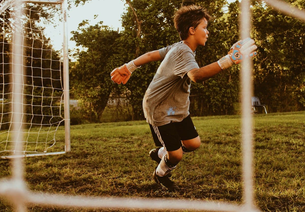 A boy in goalkeeper gloves running on a football pitch