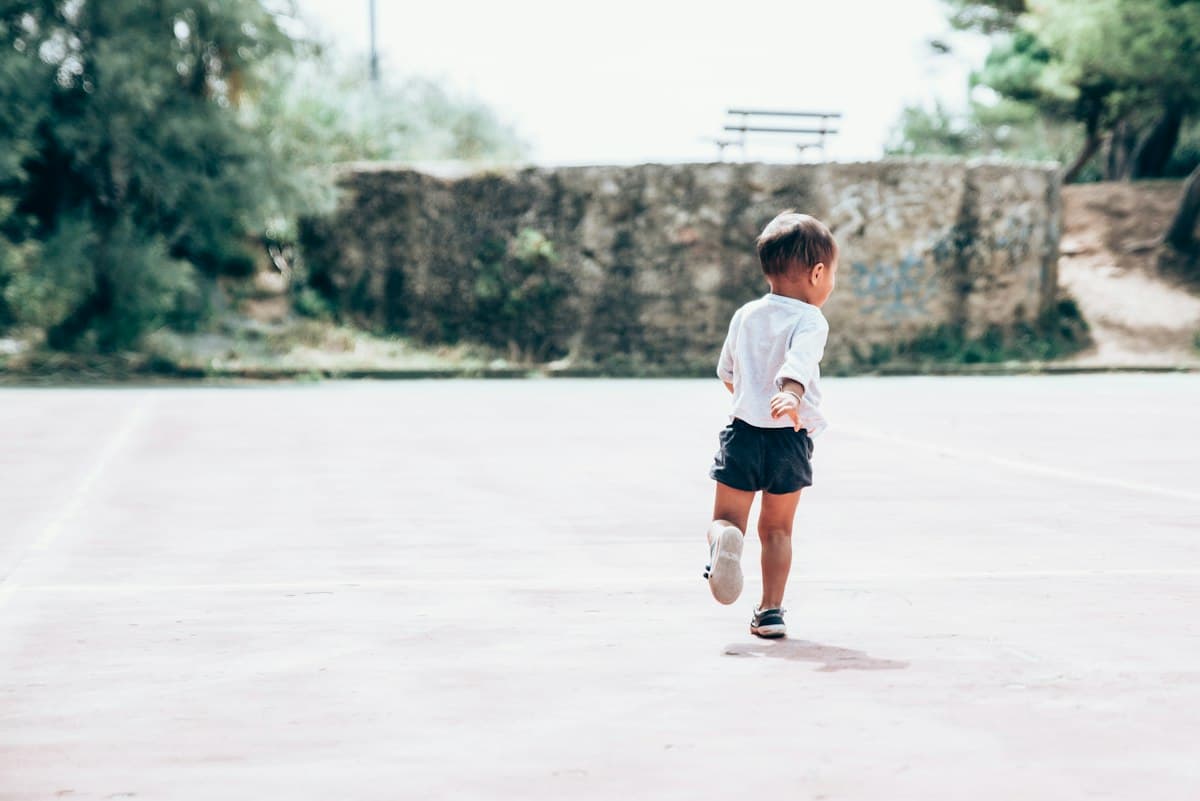 A toddler running across a playground, feet in view