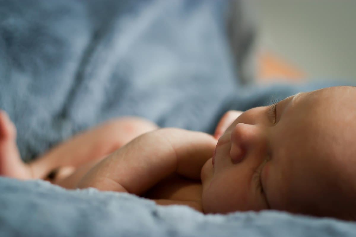 A newborn asleep on a blue blanket, head turned to one side