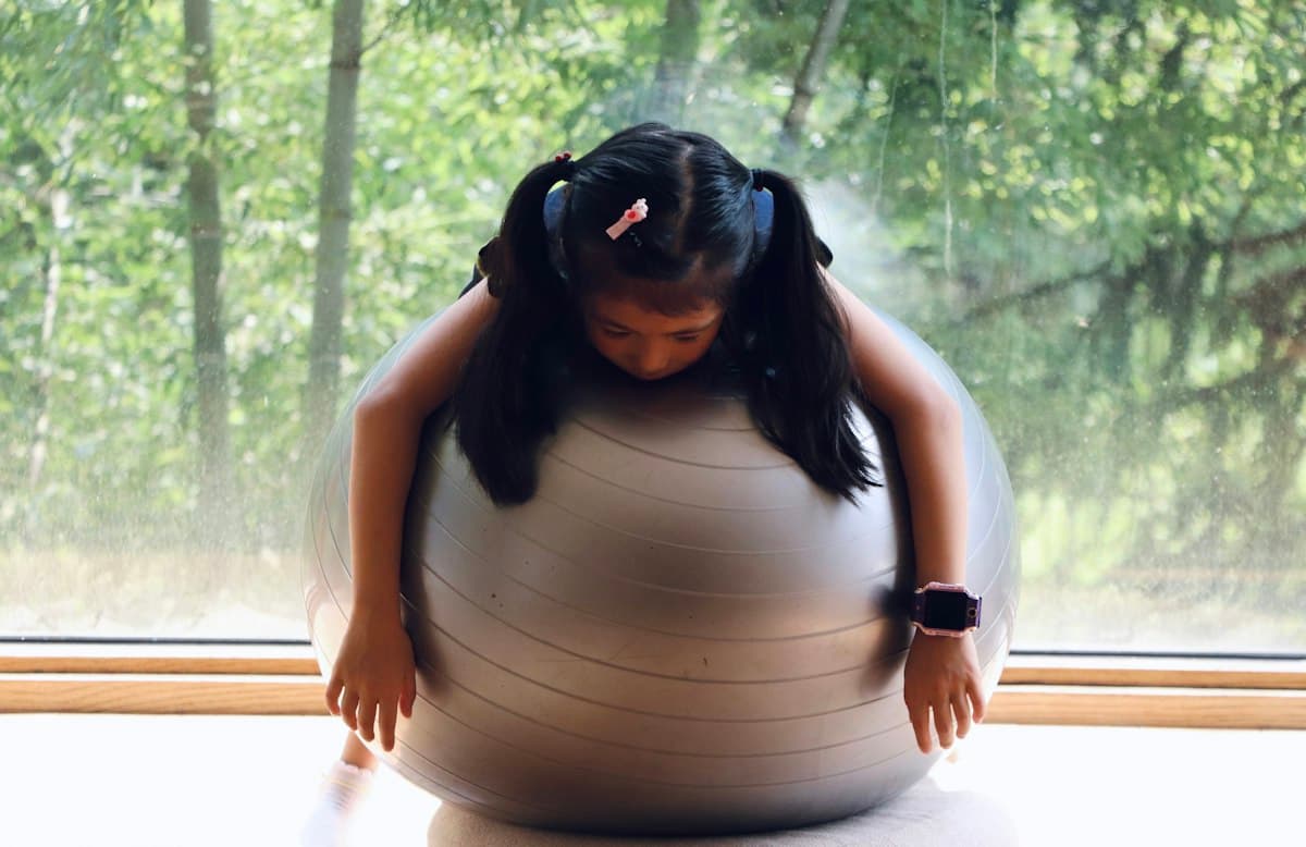 A girl stretching over a large exercise ball by a window
