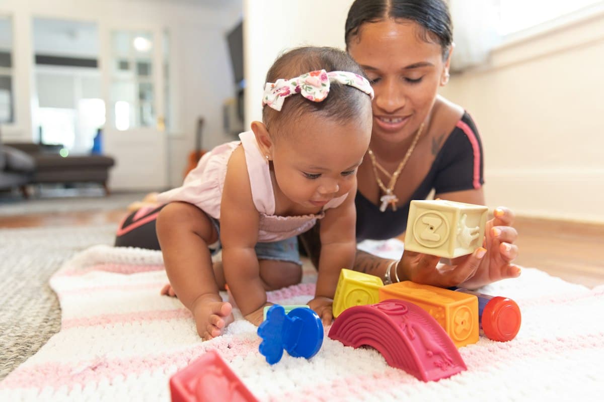 A mother and baby playing with stacking blocks on a blanket at home