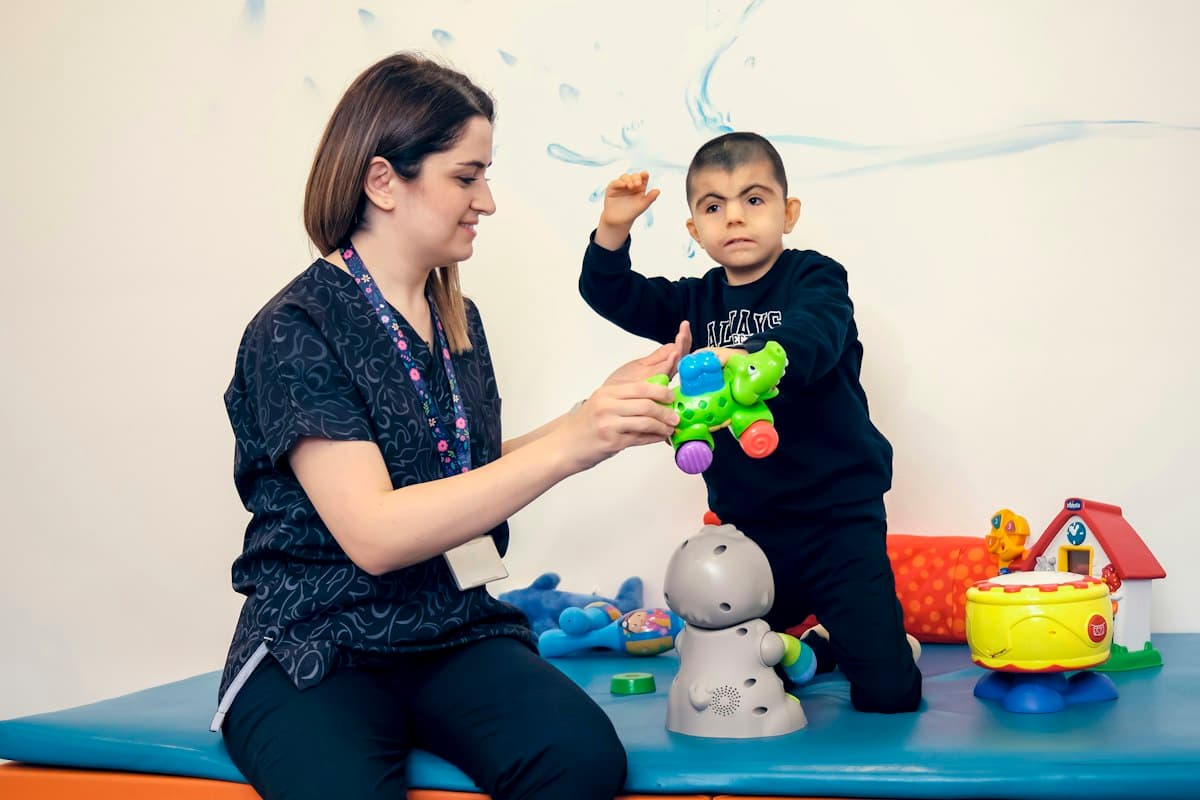 A therapist playing with a young child on a soft mat surrounded by toys