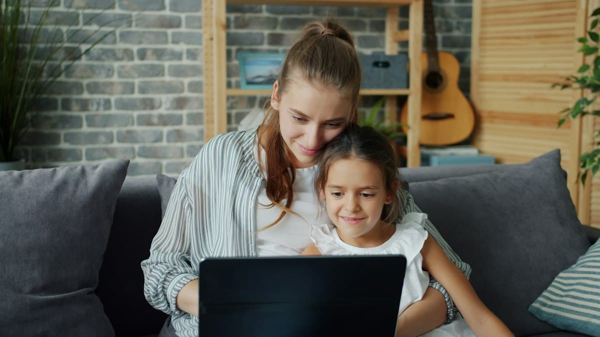 A mother and daughter looking at a laptop together on the sofa