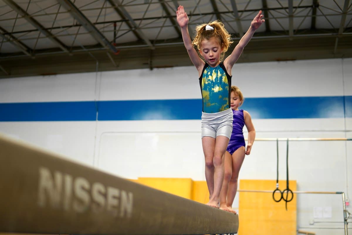 A young girl balancing on a gymnastics beam with her arms raised